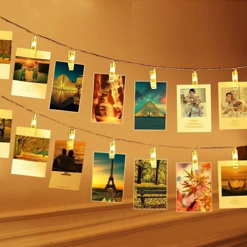 String lights with photo clips displaying various photos on a wall.