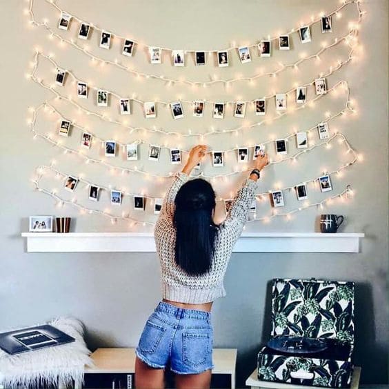 Person arranging photos on a string of lights against a wall.