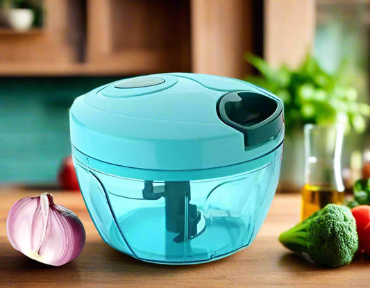 Turquoise hand chopper with vegetables in the background on a white surface