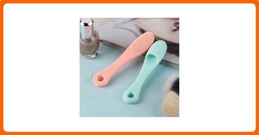 Two small brushes, one pink and one green, on a light blue surface with a blurred background.